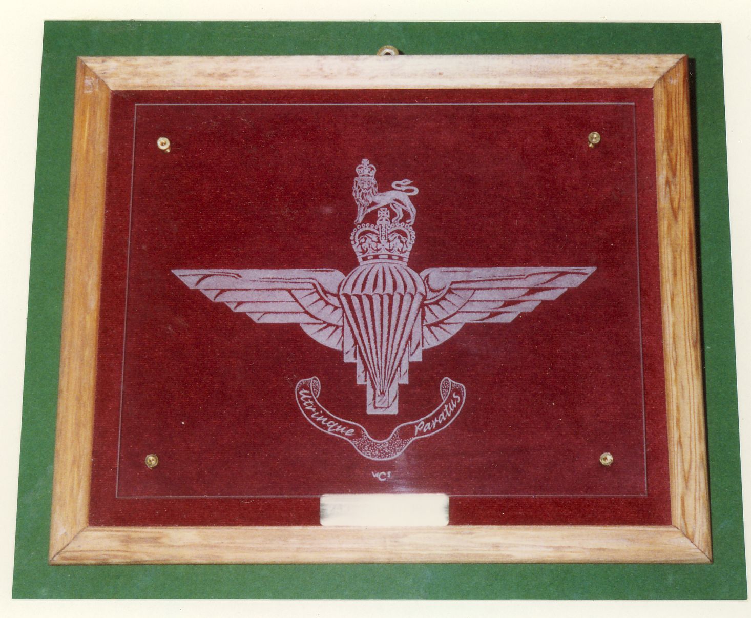 An engraving of the badge of the Parachute Regiment. On this occasion it is mounted above a maroon velvet background.