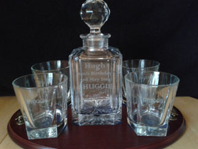 Four personal engraved crystal whisky glasses and decanter in the middle. These are sat on a polished wooden base.