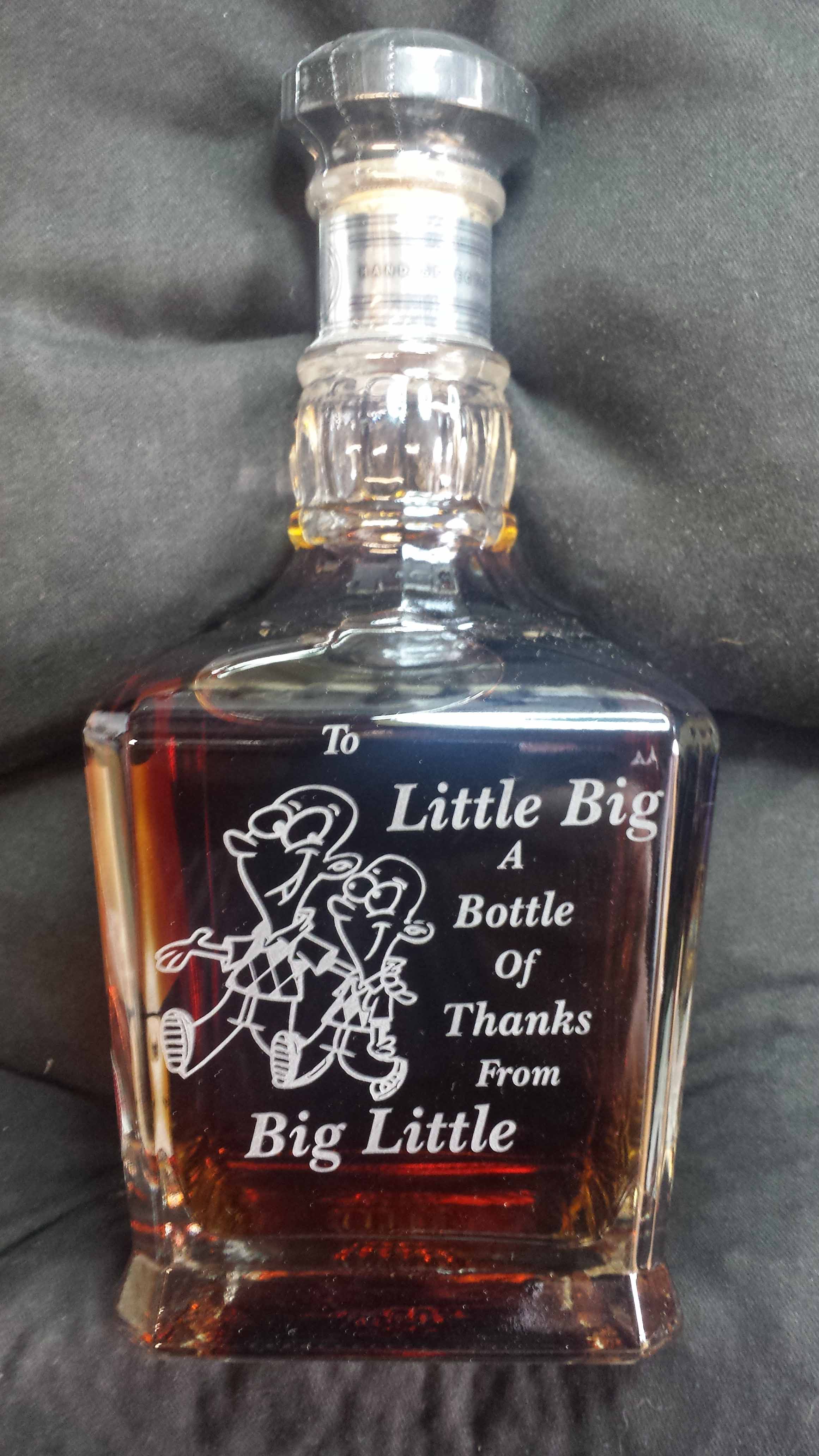 This bottle of spitits is engraves with a cartton of two men, one tall, one short and both bauld striding along together with the words 'To Little Big A Bottle Of Thanks From Big Little.